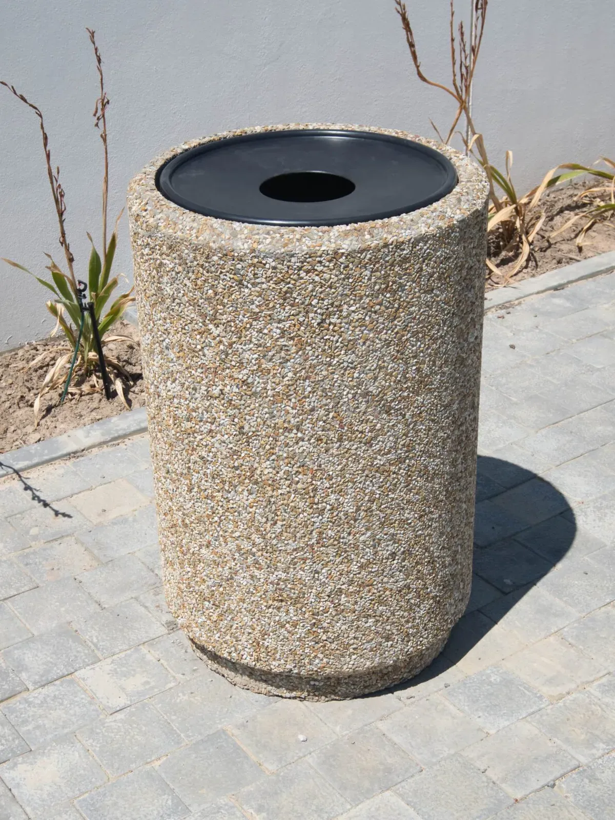 Round precast concrete litter bin with a black liner hood, installed on block paving