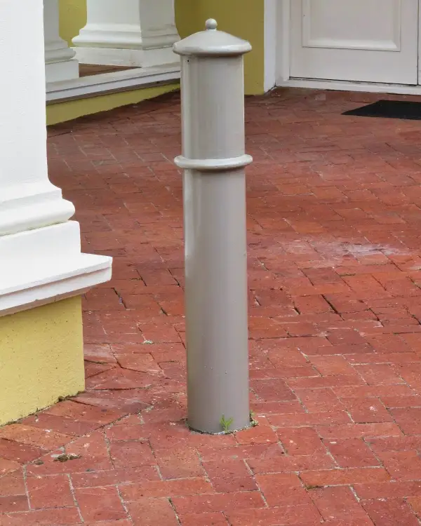 Cannon steel bollard with a domed, ball-finial cap and a raised mid-shaft band, set in brick paving at a heritage building entrance