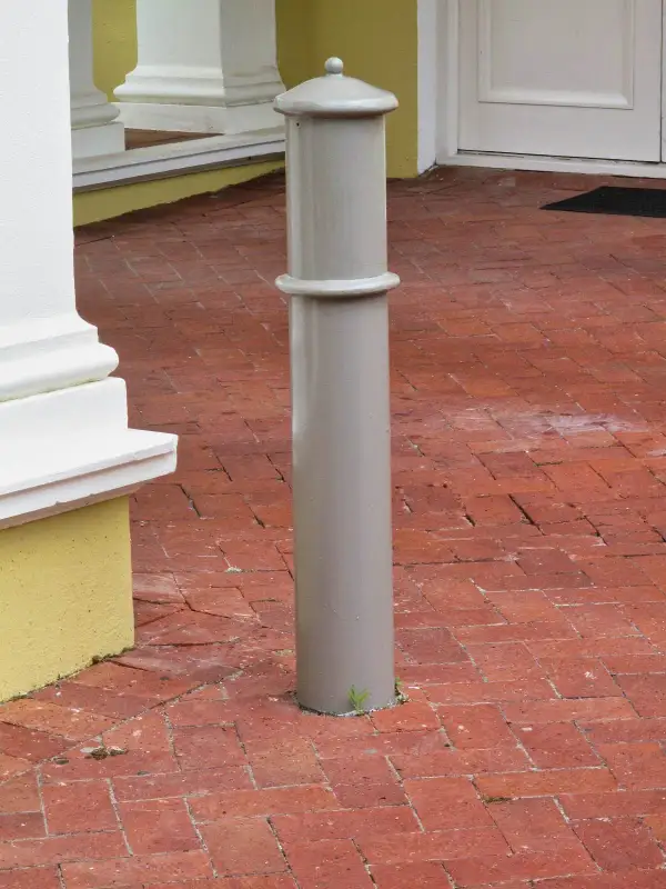 Cannon steel bollard with a domed, ball-finial cap and a raised mid-shaft band, set in brick paving at a heritage building entrance
