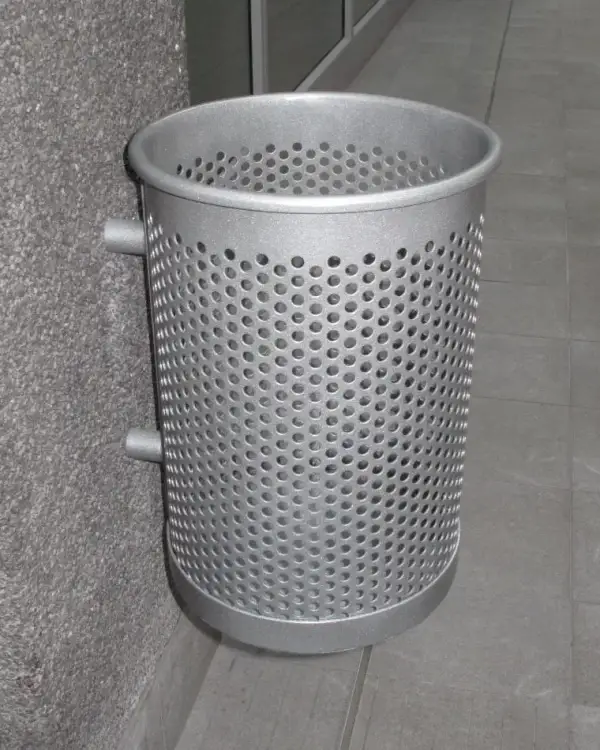 Perforated wall mounted steel bin in a silver powder-coated finish, bracketed off an exposed-aggregate concrete column and hanging clear of the floor of a covered walkway