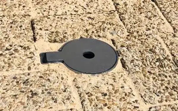Flush-mounted lockable ground sleeve lid for a removable steel bollard, set into paving