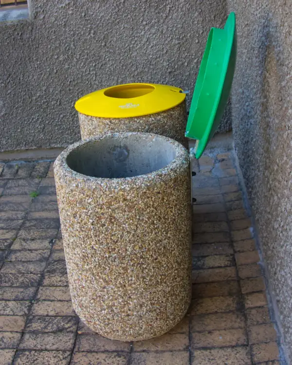 Round 500 concrete bin with a green hinged lid swung open on its bracket, a second bin with a closed yellow lid behind it