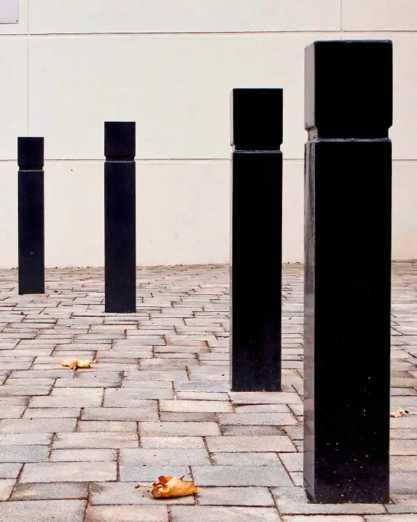 Square 150 flat-top steel bollards powder-coated black, in a line on brick paving