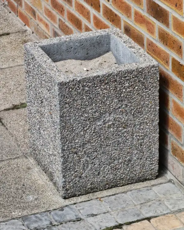 Square ash concrete bin in exposed aggregate, sand-filled, standing against a face-brick wall on setts paving