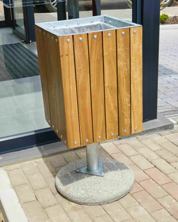 Square slatted steel bin — hardwood slats on a galvanised steel frame with a galvanised rim and liner, on a post set into a round precast concrete base, on brick paving at a building entrance