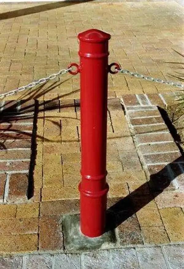 Red steel bollard with a domed cap and paired chain eyes, linked to its neighbours by a galvanised chain