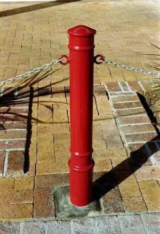 Red steel bollard with a domed cap and paired chain eyes, linked to its neighbours by a galvanised chain